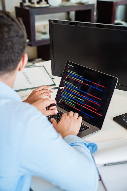 A close-up photograph of a computer screen displaying lines of programming code, illuminated with colorful syntax highlighting in shades of red, green, blue, yellow, and white. The code appears blurry